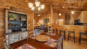 A wooden cabin interior with a dining table, chairs, a sofa, and a bar area. - Dog Friendly! Hot Tub | Gameroom (Gatlinburg)