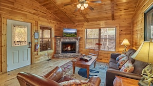 A cozy cabin interior with a stone fireplace, leather furniture, and wooden walls. - Dog Friendly! Hot Tub | Gameroom (Gatlinburg)