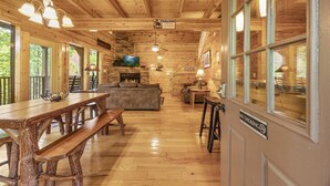 A wooden interior with a long dining table, benches, a sofa, and a fireplace.