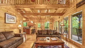 A wooden cabin interior with a sofa, coffee table, and a dining area.