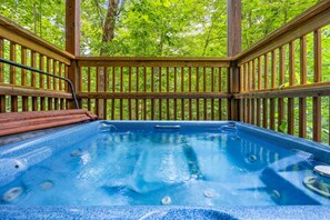 A hot tub with a wooden deck and railings, surrounded by lush greenery. - Cherokee Charm: Theater, Gameroom, Hot Tub, Sauna (Gatlinburg)