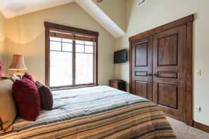 A bedroom with a large bed, a window, a TV, and wooden doors.
