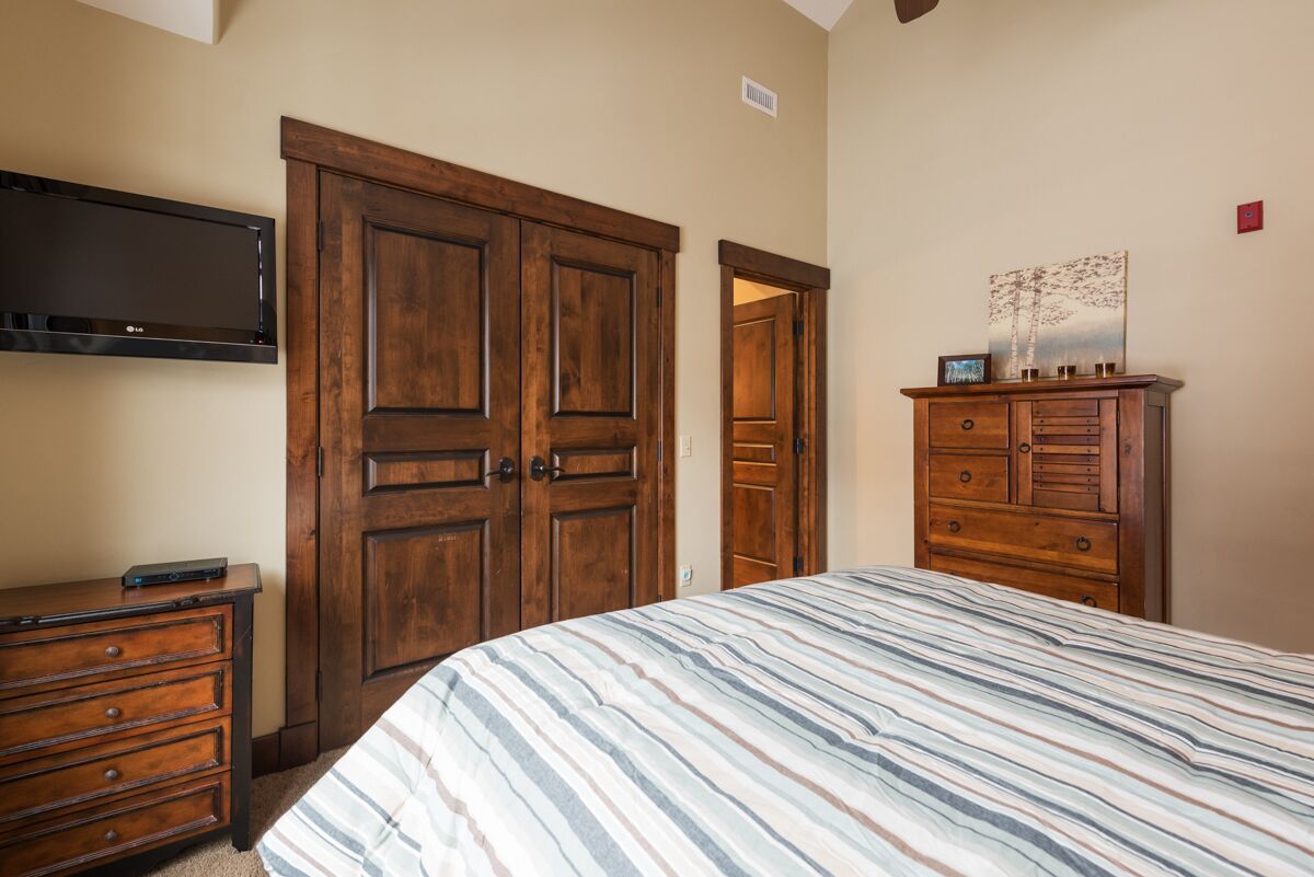 Een slaapkamer met een groot bed, een houten kledingkast en een flatscreen televisie aan de muur.