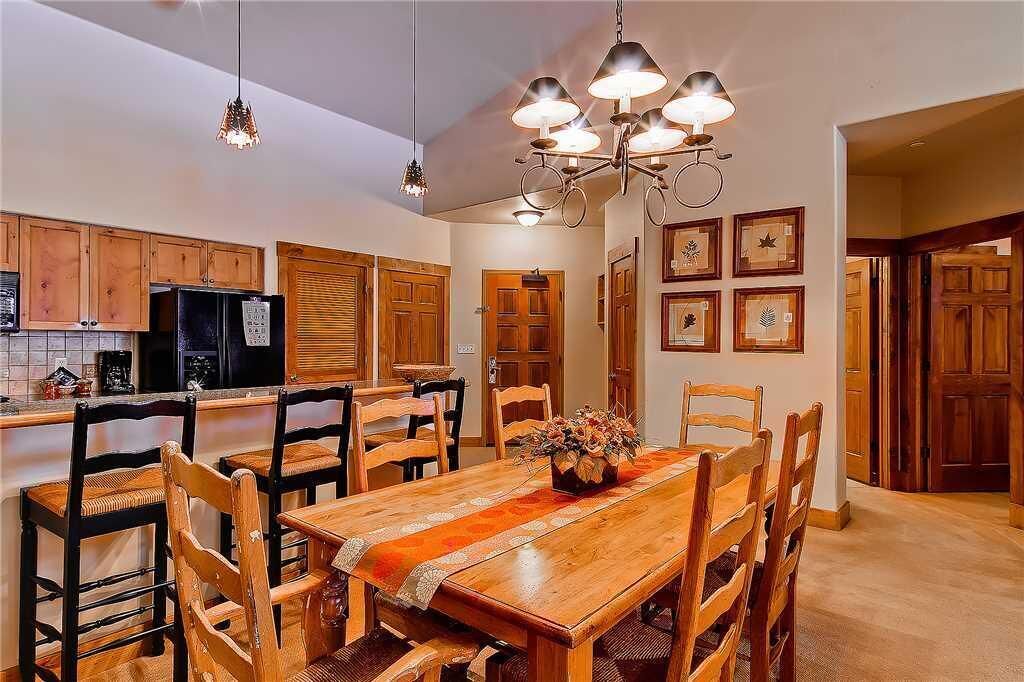 Een keuken met houten kastjes, een zwarte koelkast en een eethoek met een houten tafel en stoelen.