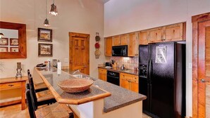 Una cocina con armarios de madera, un refrigerador negro, un microondas y un comedor con una isla grande y sillas.