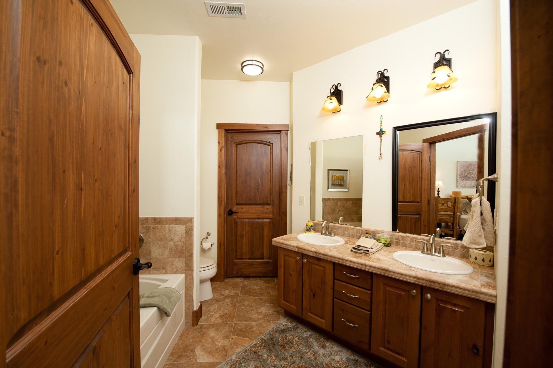 Une salle de bain avec des meubles en bois, un meuble-lavabo à deux vasques, une baignoire et un grand miroir.
