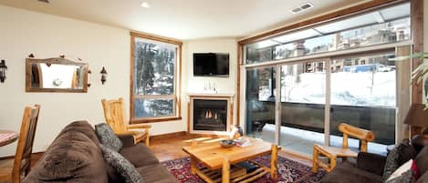 A cozy living room with a fireplace, large windows, and a view of a snowy landscape.