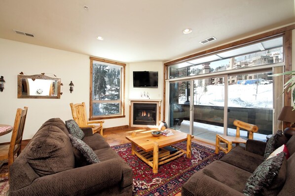 A cozy living room with a fireplace, large windows, and a view of a snowy landscape.