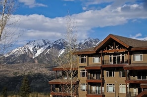 A multi-story building with balconies, set against a backdrop of snow-capped mountains and clear skies.