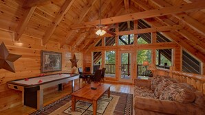 A cozy wooden cabin interior with a pool table, a sofa, and a dining table.