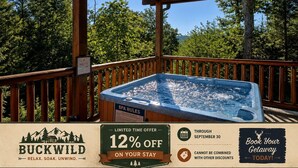 A wooden deck with a hot tub, surrounded by trees, and a sign offering a 12% discount on stays.