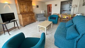 A living room with a television, wooden cabinet, blue armchairs, a grey sofa, and a small table.