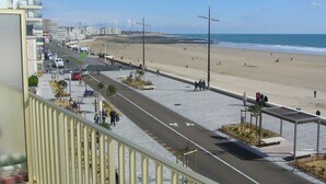 A coastal road with a beach in the background, pedestrian paths, and a row of buildings.