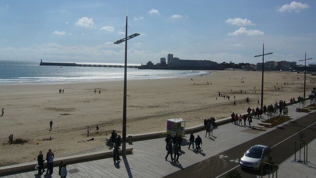A beach with a promenade, a few people, and a distant pier.