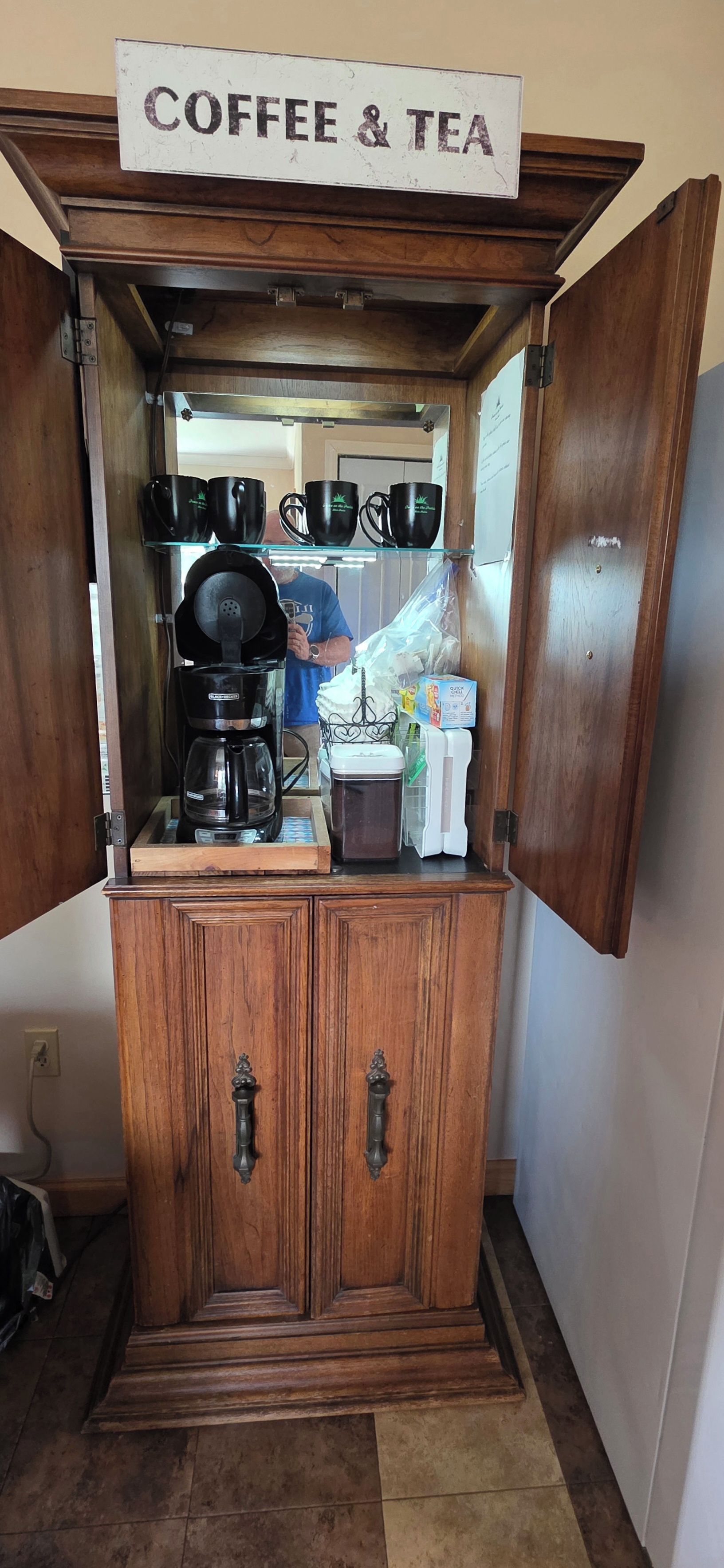 A coffee and tea station with a coffee maker, mugs, and a tea kettle.