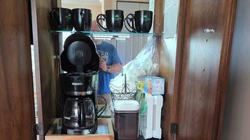 A coffee and tea station with a coffee maker, mugs, and a tea kettle.