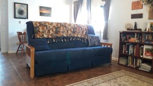 A living room with a blue sofa, a patterned throw, a wooden side table, a bookshelf, and a patterned rug.