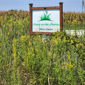 A sign with the text 'Peace on the Prairie' and 'Klein Prairie' surrounded by tall grasses and wildflowers. - Peace on the Prairie — Quiet Nature Retreat on 23 Acres (Murrayville)