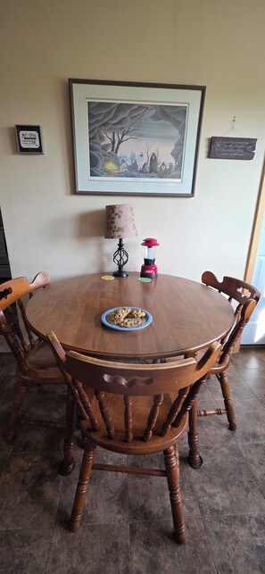 A round wooden dining table with a plate of cookies, surrounded by wooden chairs. - Peace on the Prairie — Quiet Nature Retreat on 23 Acres (Murrayville)