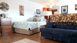 A room with a bed, a blue sofa, a wooden dresser, and a patterned rug.