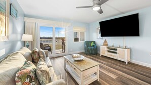 A living room with a sofa, coffee table, TV, and a ceiling fan. - 117- Beach Level Delight, Walk out to the Beach or Pool, Free Beach Service (Destin)