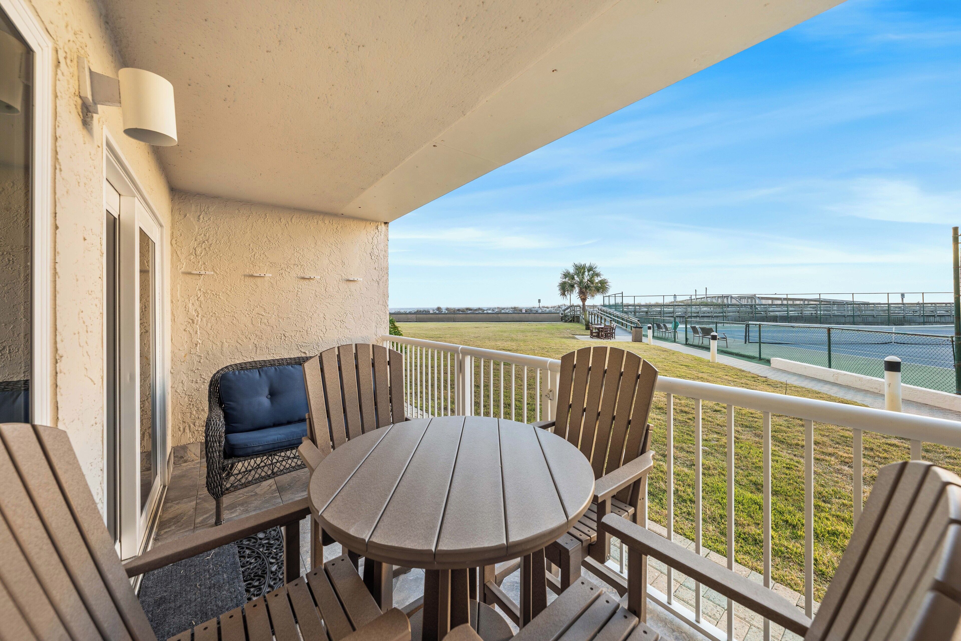 A balcony with a round table and chairs, a view of a marina, and a palm tree in the distance.