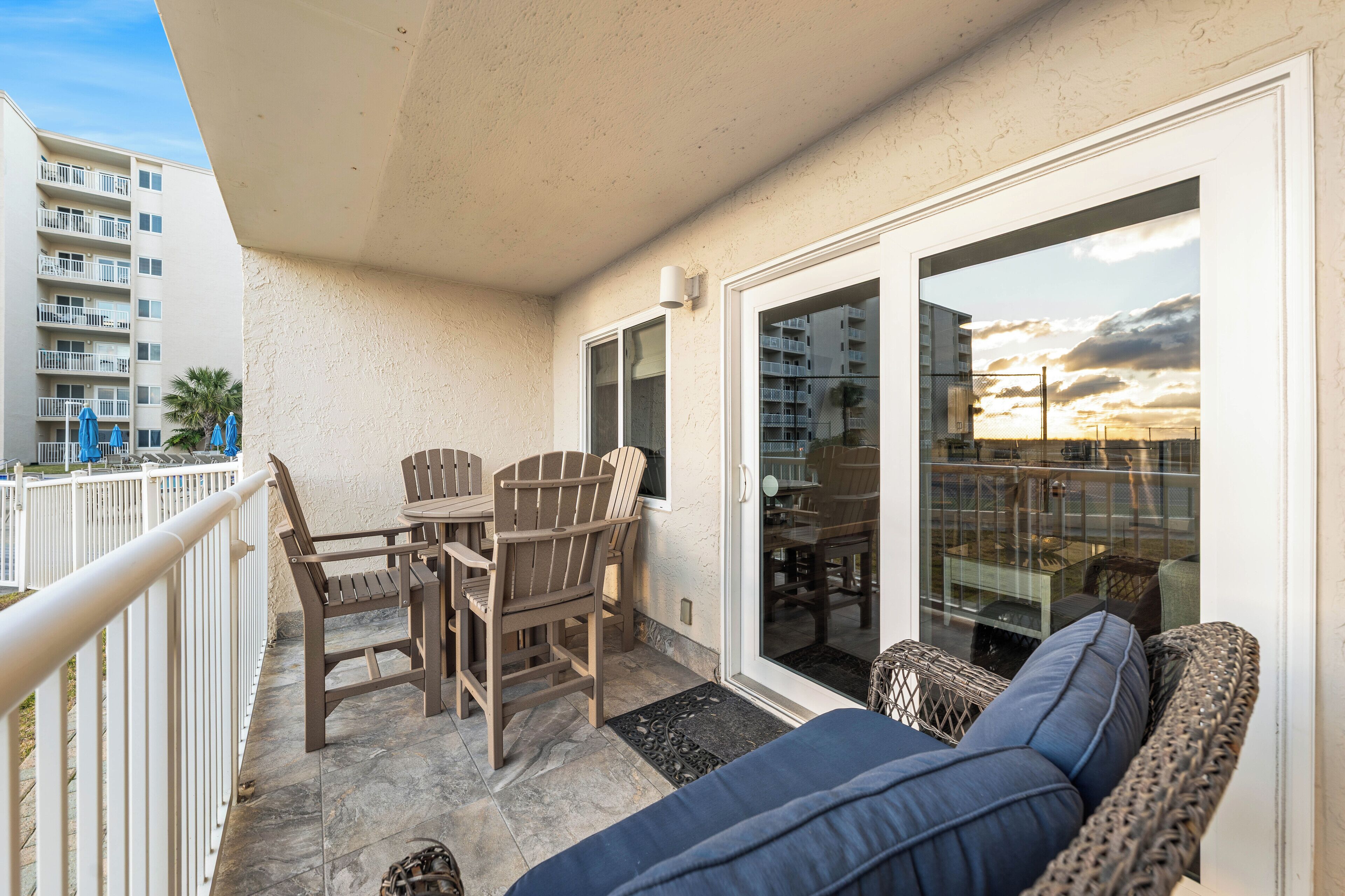 A balcony with a table and chairs, a sofa, and a sliding glass door leading to an indoor area.