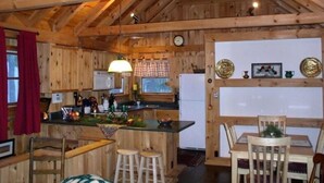 Una cabaña rústica de madera con cocina, comedor y un amplio techo de madera.