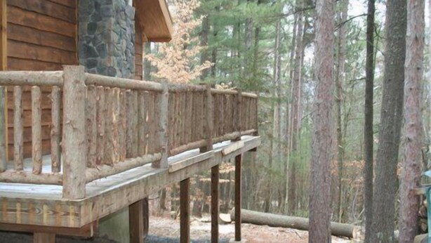 Una terraza de madera con un muro de piedra y barandilla de madera, rodeada por un bosque.