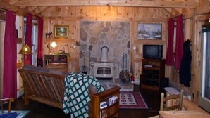 Un interior de cabaña acogedor con chimenea de piedra, mobiliario de madera y un televisor.