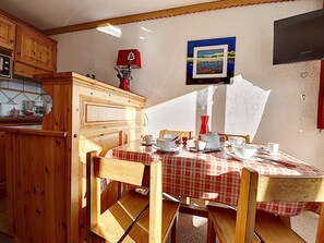 Une cuisine chaleureuse avec des meubles en bois, une table à manger recouverte d’une nappe à carreaux rouges et blancs, et un tableau accroché au mur.
