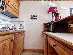 Une cuisine compacte avec des meubles de rangement en bois, un four à micro-ondes et une machine à café posés sur le plan de travail.