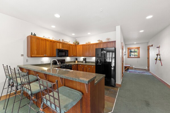 A modern kitchen with wooden cabinets, a central island, bar stools, and a refrigerator. - Spacious Townhouse in River Run w/ Slope Views from Private Deck! (Keystone)