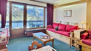 A cozy room with a red sofa, a dining table with chairs, and a view of mountains through large windows. - Studio for 4 in Tignes ski-in/ski-out near shops (Tignes)
