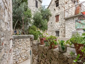 A narrow stone-walled alley with potted plants and a stone building with a balcony.