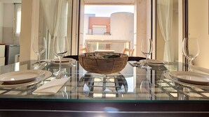Un coin repas avec une table en verre mise pour quatre personnes, comprenant des assiettes, des couverts et des verres à vin. Un panier en osier est posé sur la table.