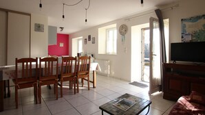 A spacious living area with a dining table and chairs, a television, and a tiled floor.