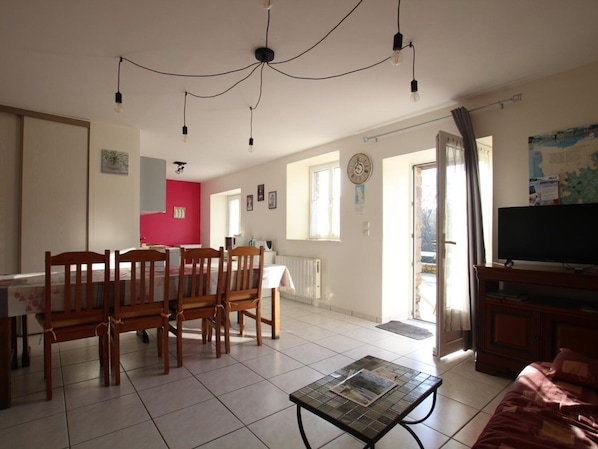 A spacious living area with a dining table and chairs, a television, and a tiled floor.