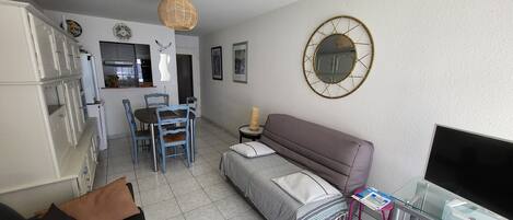 A compact living space with a kitchenette, dining area, and a sofa with a TV stand.