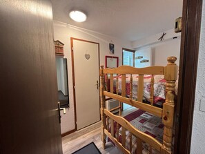 A bedroom with a wooden bed frame, a door with a heart-shaped decoration, and a small window.