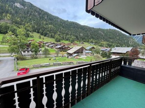 Un balcon donnant sur un village de montagne, avec des bâtiments en bois et une voiture rouge garée à l’extérieur.
