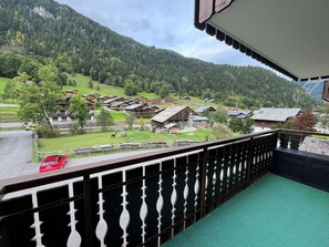 A balcony with a view of a mountain village, wooden buildings, and a red car parked outside.