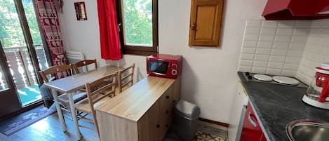 A compact kitchen with a dining area, a microwave, a sink, and a window with curtains.