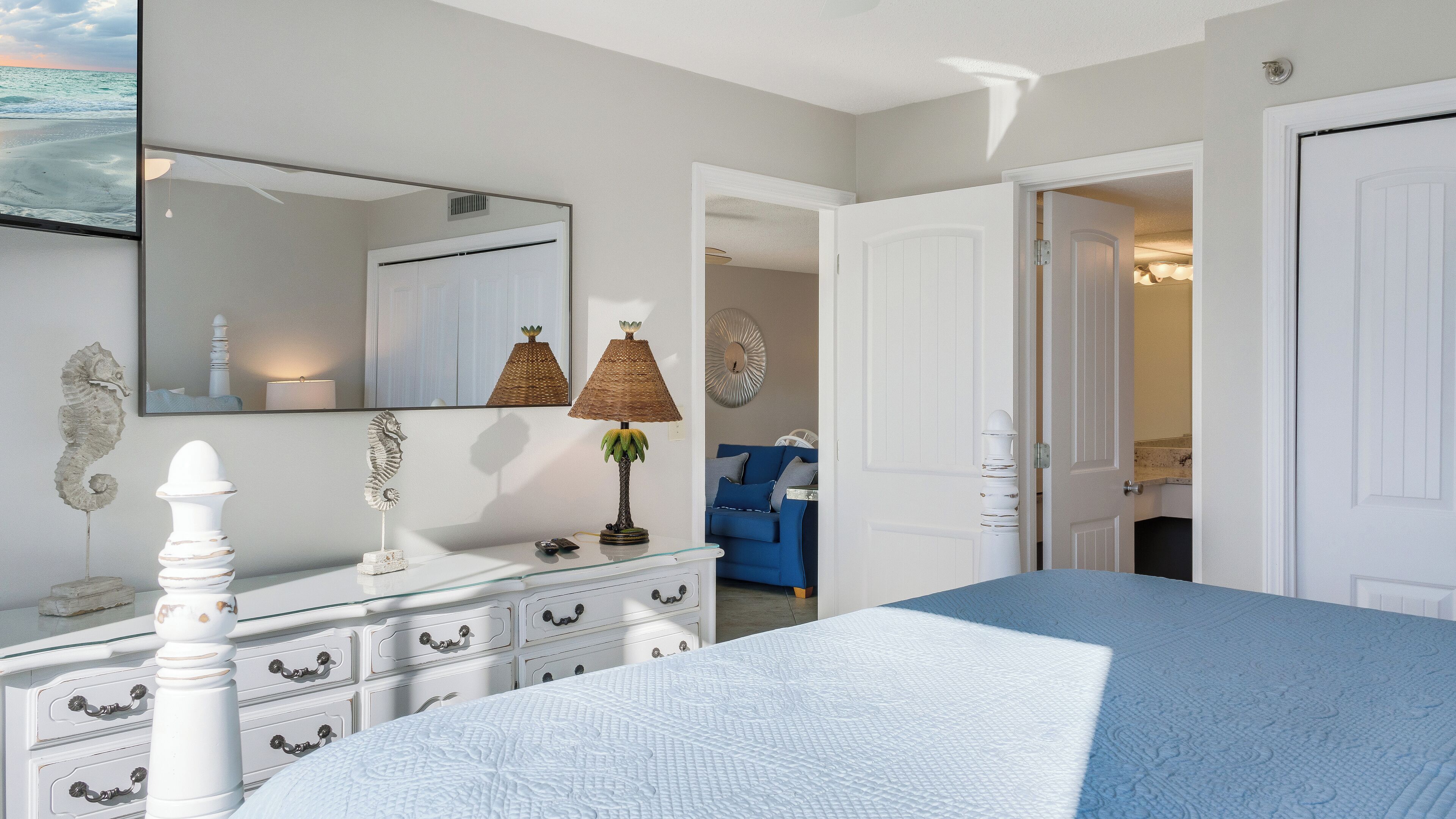 Un dormitorio con cama, cómoda, espejo y vista al mar por una ventana.
