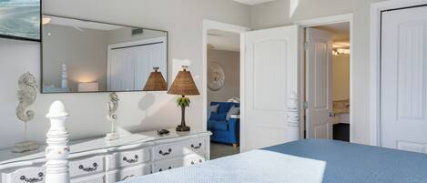 Un dormitorio con cama, cómoda, espejo y vista al mar por una ventana.