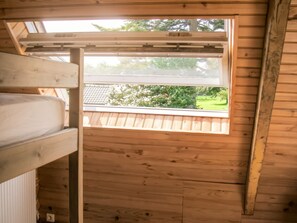 A room with a bunk bed, a window with a view of a garden, and wooden walls.