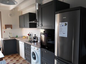 A modern kitchen with stainless steel appliances, a Bosch washing machine, and a refrigerator with a note attached.
