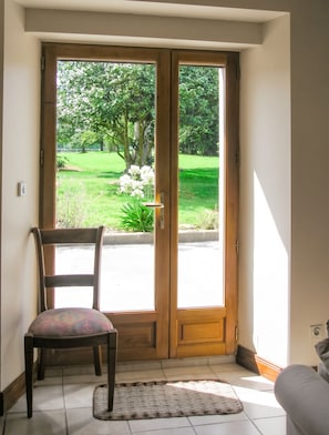 Een kamer met een stoel en een vloerkleed, een houten deur die uitkomt in een tuin.
