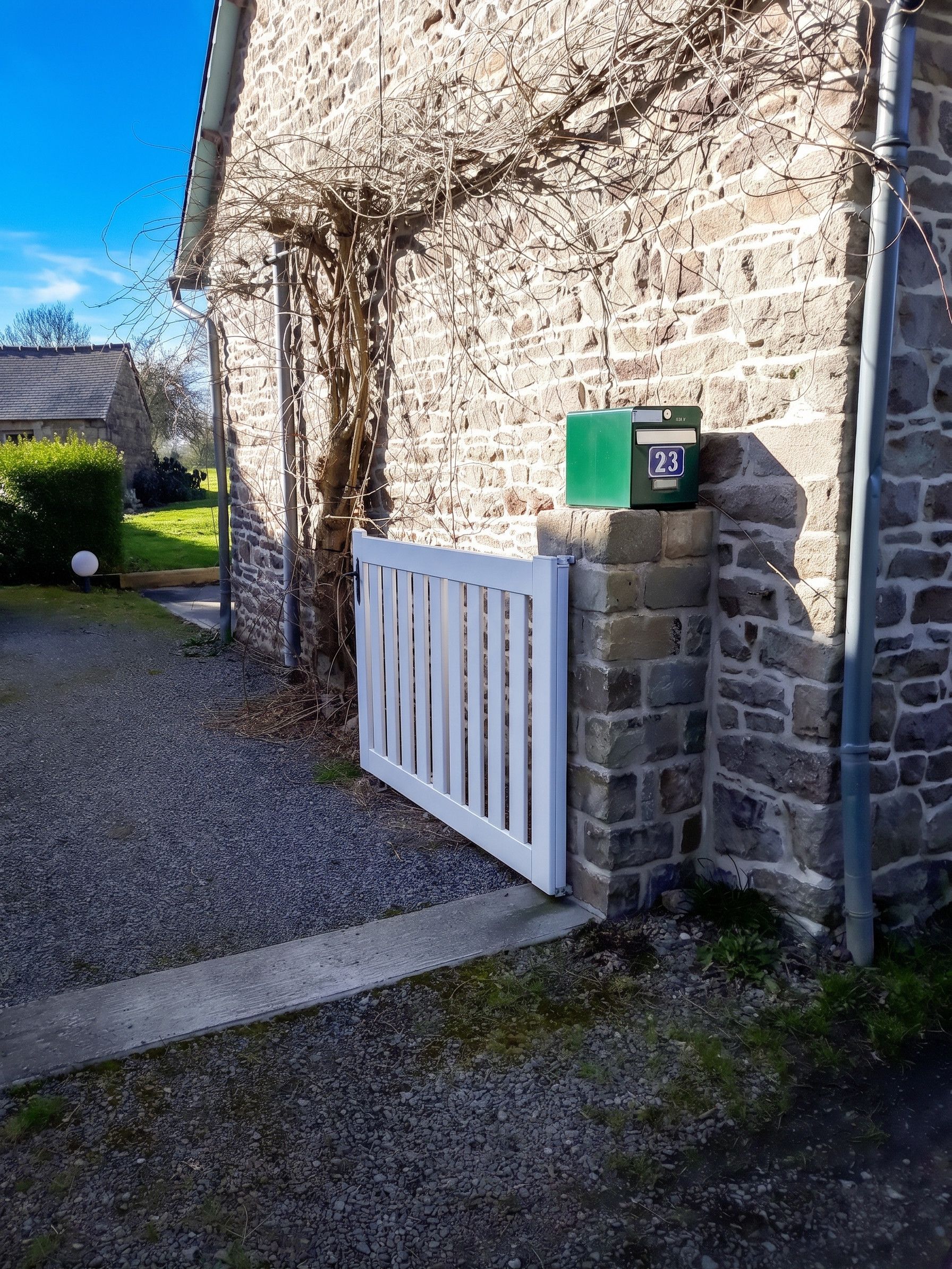A stone building with a white gate, a mailbox, and a clear sky.