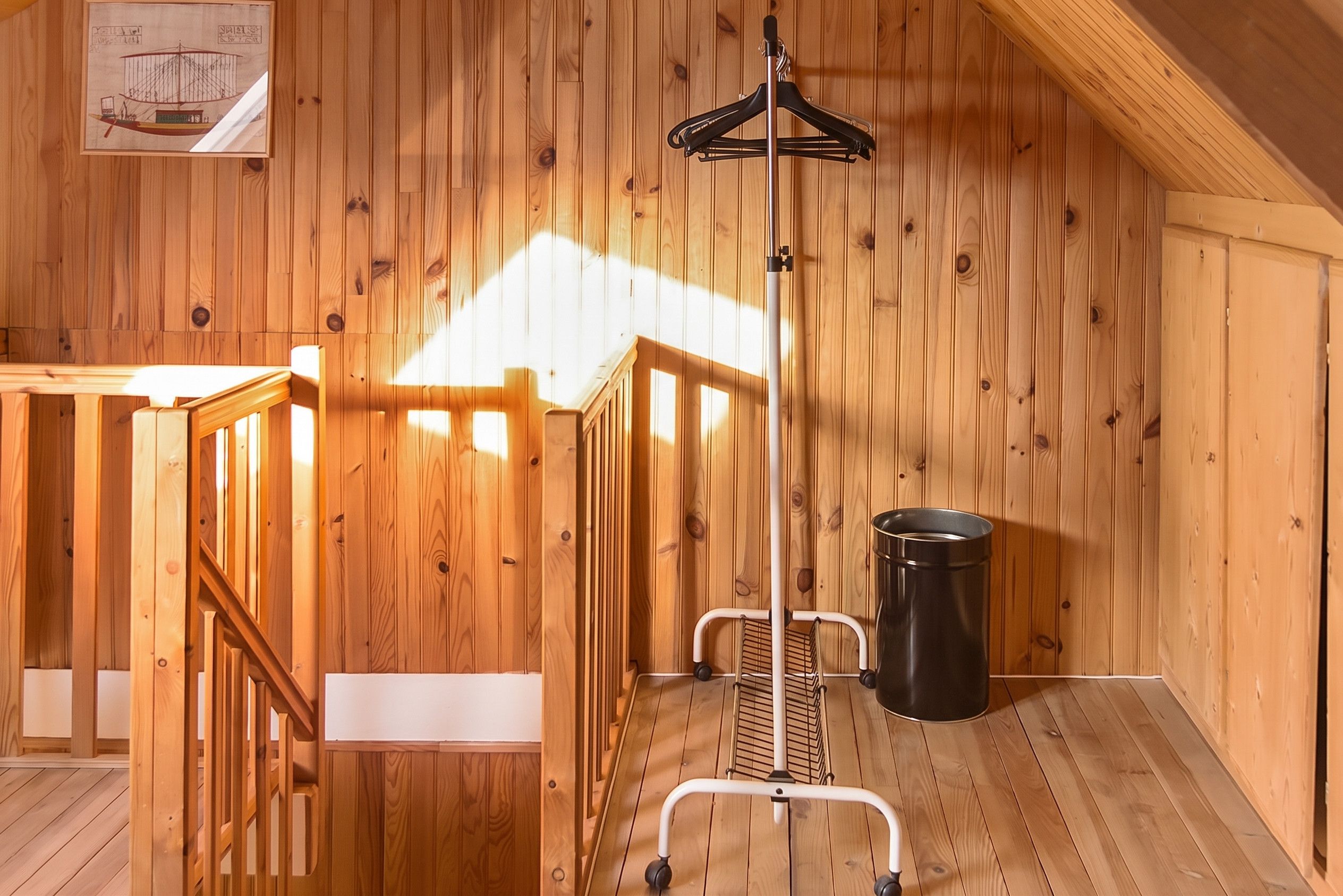 A wooden interior with a metal rack, a trash bin, and a white bench.